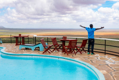 A man standing next to a swimming pool against a scenic lookout at tsavo east national park in kenya