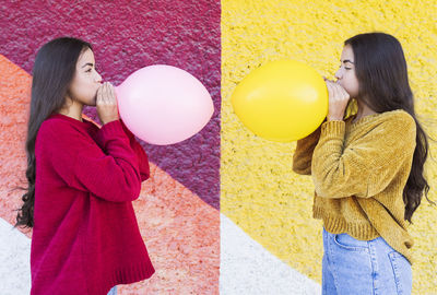 Playful sisters blowing up balloon next to multi colored wall