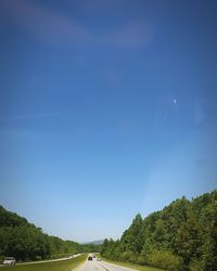 Road amidst trees against clear blue sky