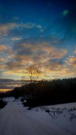 Snow covered landscape against sky during sunset