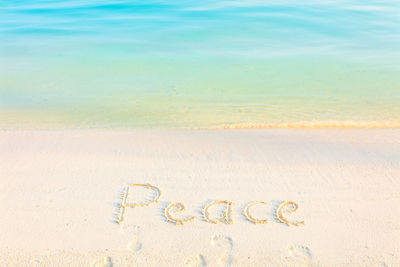 High angle view of peace text on sand at beach