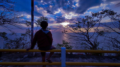 Man standing by railing against sky during sunset