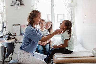 Female doctor examining throat of girl while family sitting in medical room