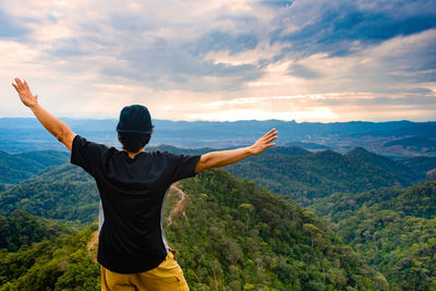 Rear view of man with arms outstretched standing against sky