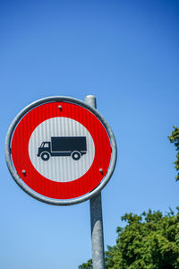 Low angle view of road sign against clear blue sky