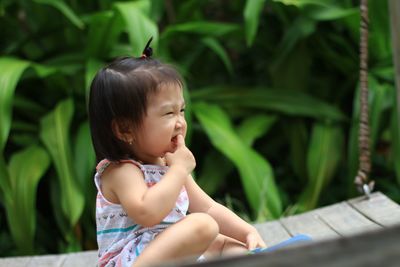 Cute girl with finger in mouth sitting on swing at park