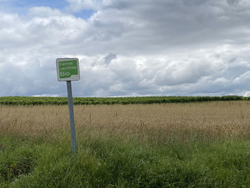 Road sign on field against sky