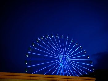 Low angle view of illuminated ferris wheel against clear blue sky