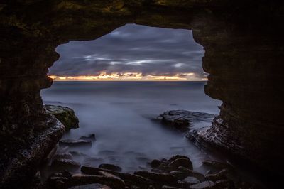 Scenic view of seascape against cloudy sky seen through cave during sunset