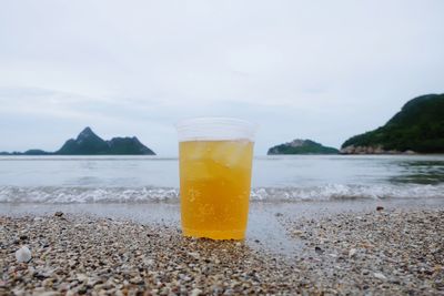 Close-up of drink in glass on shore at beach against sky