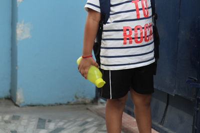 Midsection of boy holding water bottle while standing against wall