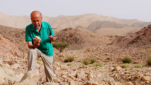 Senior man examines a stone in the desert 