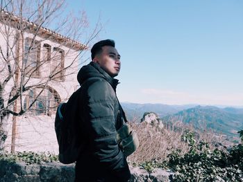 Side view of young man looking away against sky