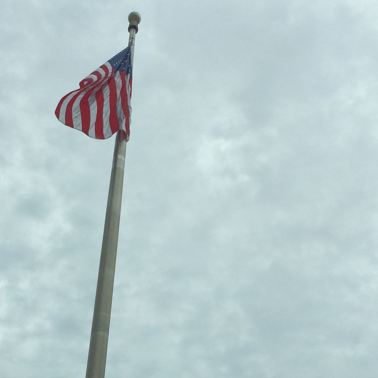 low angle view, sky, flag, patriotism, national flag, identity, pole, cloud - sky, american flag, cloud, wind, cloudy, day, red, outdoors, built structure, no people, pride, hanging, culture