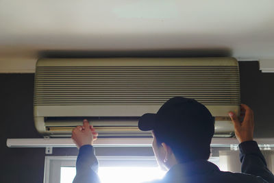 Rear view of man sitting on window at home