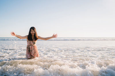 Young woman with arms raised on beach against sky