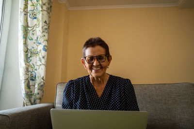 Smiling senior woman sitting at home office workplace looking in laptop.