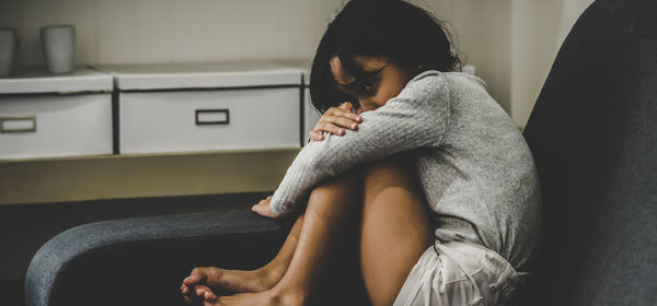 Scared girl sitting on sofa at home