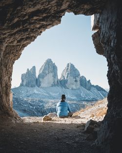 Rear view of man sitting on rock while looking at mountains