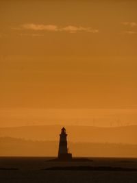 Lighthouse by sea against sky during sunset