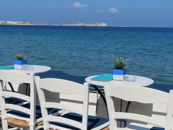 Empty chairs and tables by sea against sky