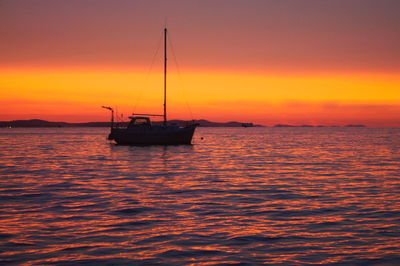 Silhouette boat sailing on sea against orange sky