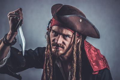 Portrait of young man in costume holding knife against gray background