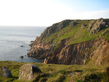 Scenic view of cliff and sea against sky on a sunny afternoon near sennen, uk