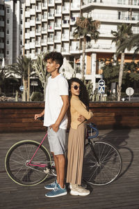 Cool couple with bicycle in the city, standing back to back