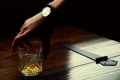 Cropped hand holding whiskey glass on wooden table