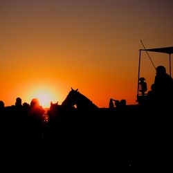 Silhouette people on land against sky during sunset