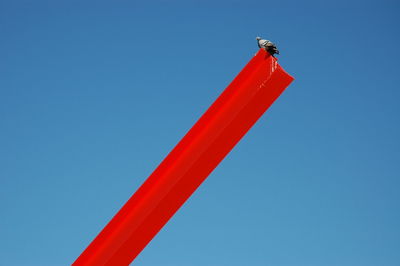 Low angle view of bird on red pole against clear sky