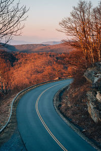 Road by trees against sky during sunset