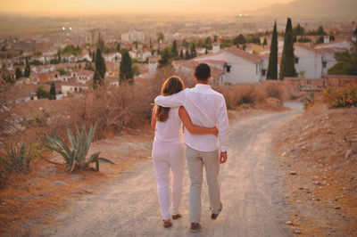 Full length of young couple on dirt road in city at sunset