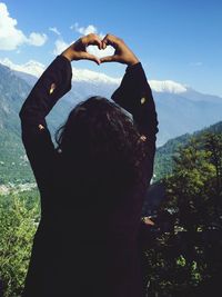 Rear view of woman standing by heart shape against sky
