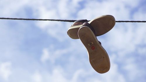 Low angle view of shoes hanging on cable against sky