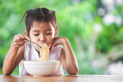 Cute girl eating noodles at table in public park