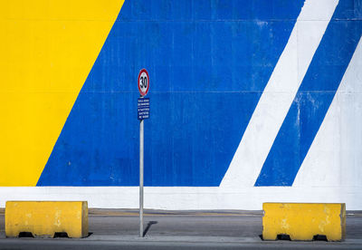 A traffic sign stands in front of a colourful wall in blue and yellow