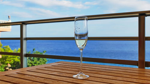 Glass of water on table by sea against sky