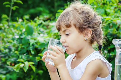 Young woman drinking water against plants