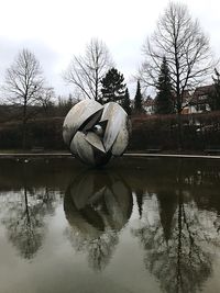Swan on bare tree by lake against sky