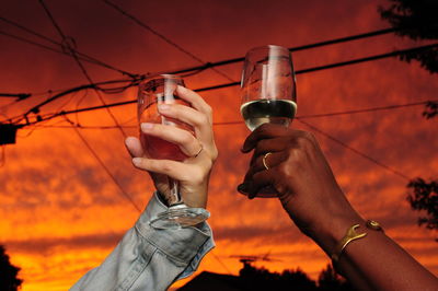 Low angle view of hand holding wine glass against orange sky