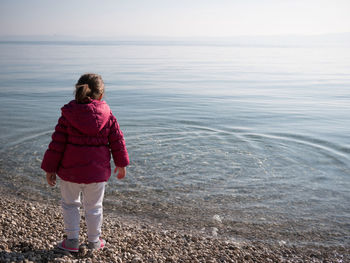 Rear view of girl wearing hooded shirt standing on sea shore at beach