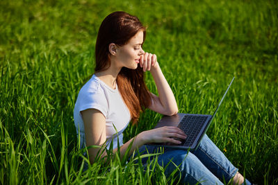 Young woman using laptop while sitting on field