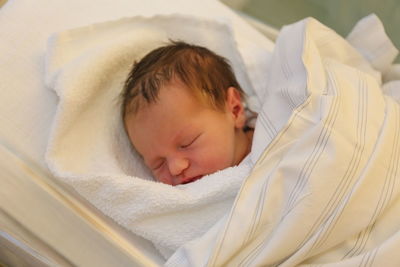 High angle view of baby wrapped in blanket while sleeping on bed