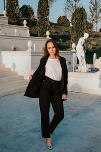 Young woman in black trouser suit and silver shoes on the background of the park