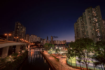 Illuminated buildings by river against sky in city at night