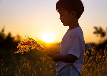 Boy standing on field against sky during sunset