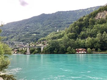 Scenic view of river by tree mountains against sky