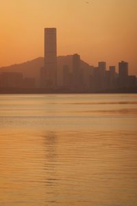 Scenic view of sea by buildings against orange sky